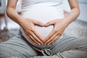Bauch einer Schwangeren mit aus Händen geformtem Herz