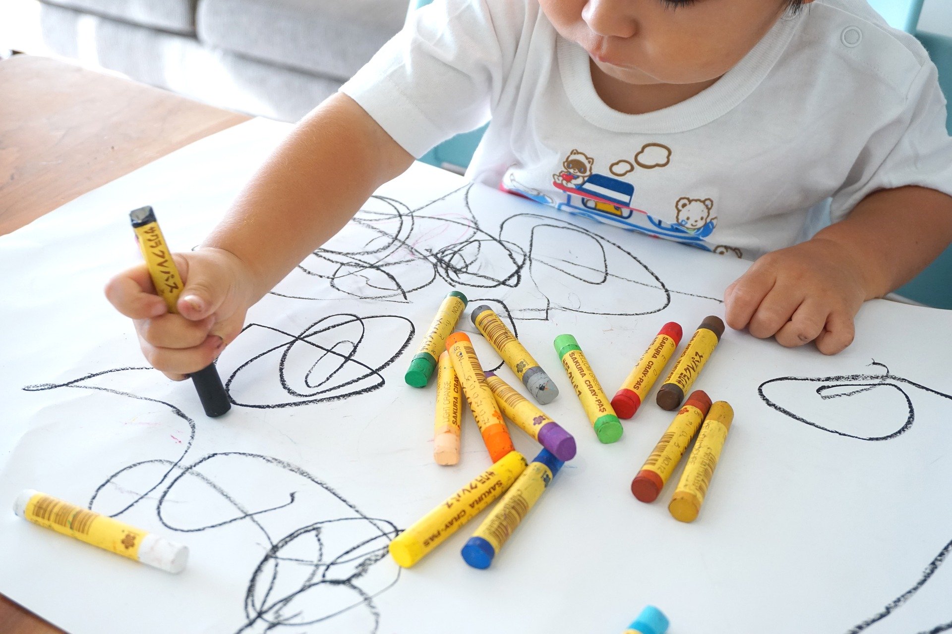 Kind malt mit Kreidestiften auf weisses Blatt