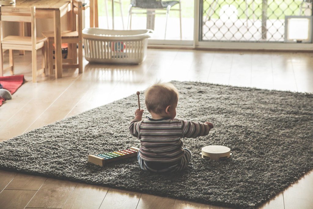 Baby sitzt auf Teppich im Zimmer und trommelt